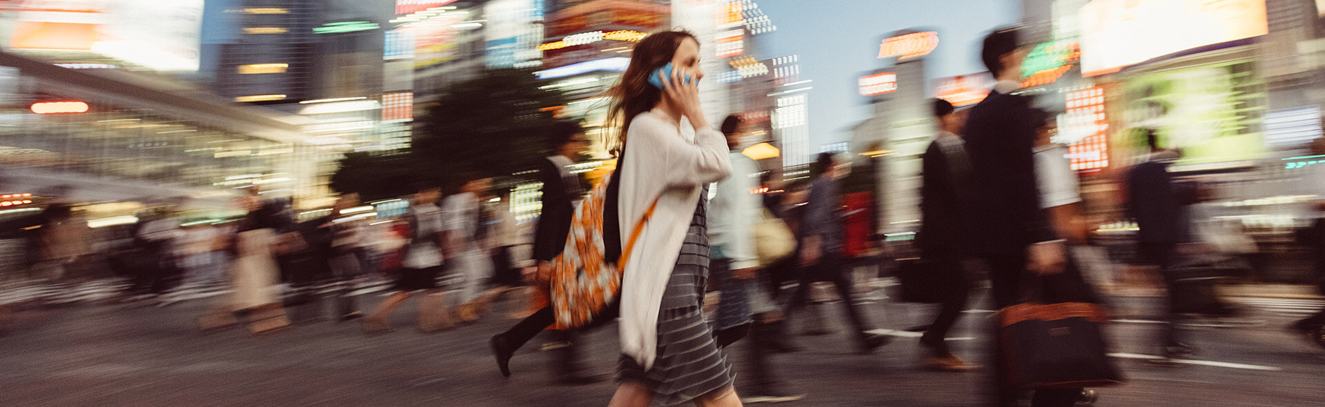 Kvinna på telefon korsar gatan i en storstad med många andra människor